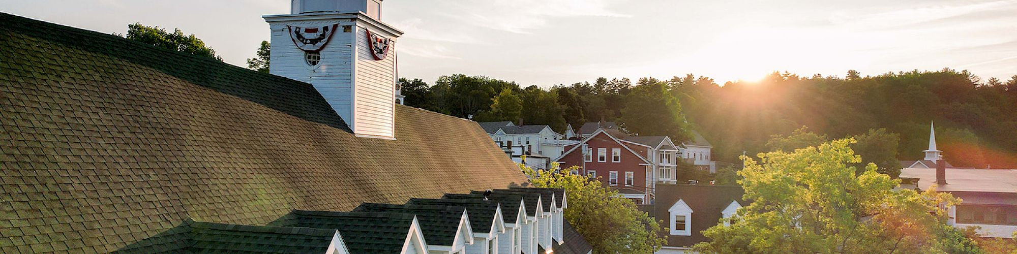 A sunlit resort hotel roof with dormer windows, a white cupola, and a town skyline beyond, basking in warm evening light.