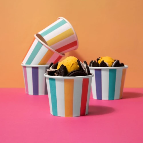 Striped cups against a colorful background, one filled with orange ice cream and cookies, others are empty and stacked.