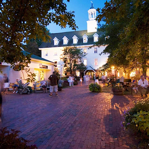 A charming courtyard scene with people enjoying a relaxed evening, surrounded by lit buildings and trees.