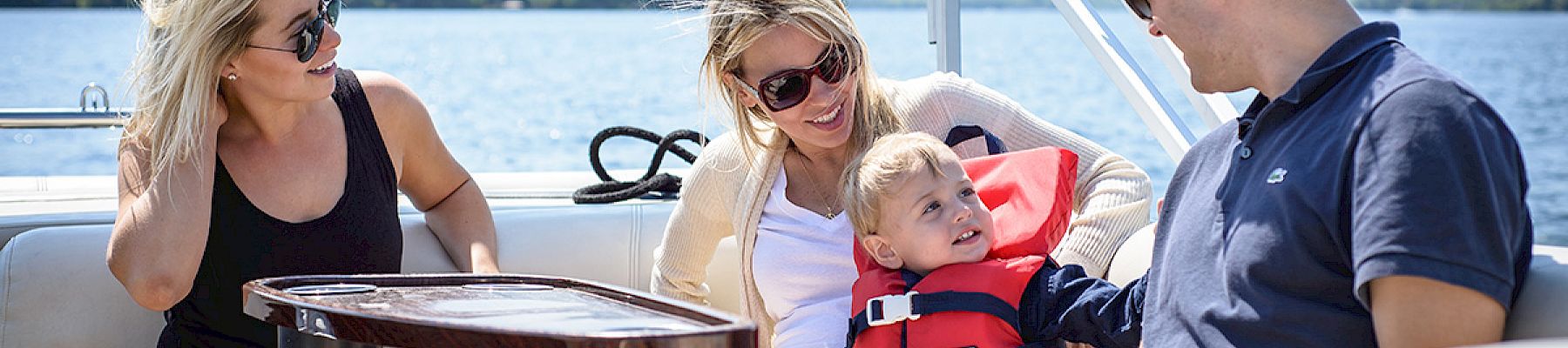 A group of people, including a child in a life vest, are sitting and relaxing on a boat, enjoying a sunny day.