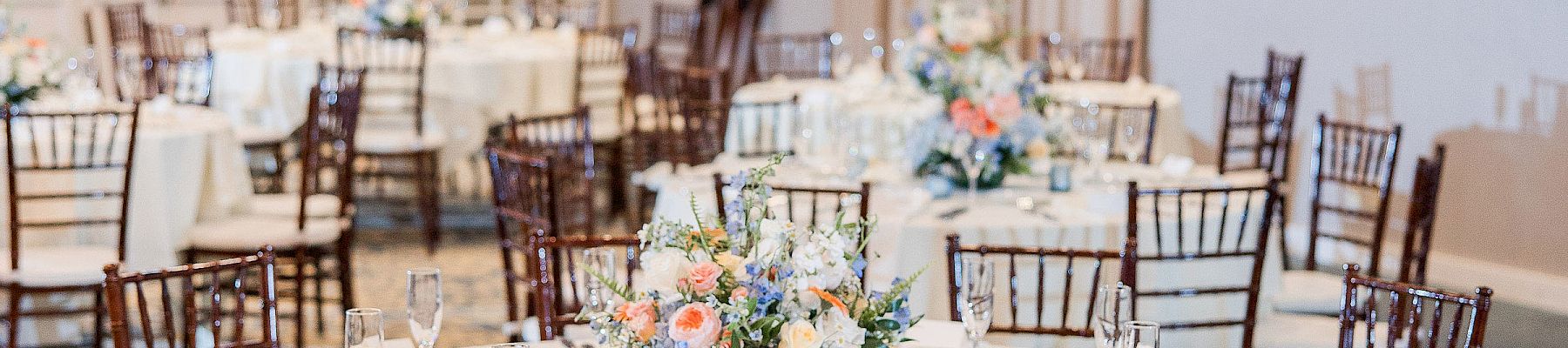 An elegantly set dining area with round tables, floral centerpieces, and wooden chairs, ready for an event or gathering.
