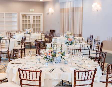 An elegantly set dining area with round tables, floral centerpieces, and wooden chairs, ready for an event or gathering.
