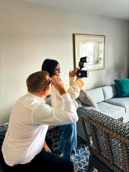 A person looking through a camera indoors, in a cozy hotel room with a sofa, and sunlight streaming in.