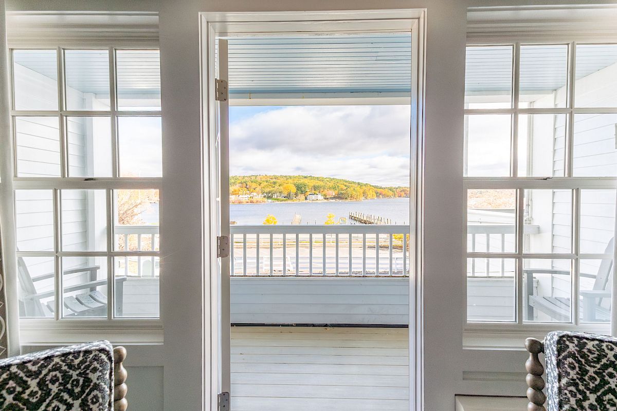 View through open patio doors reveals a serene outdoor scene with water, distant hills, and partial chairs on a sunny day.