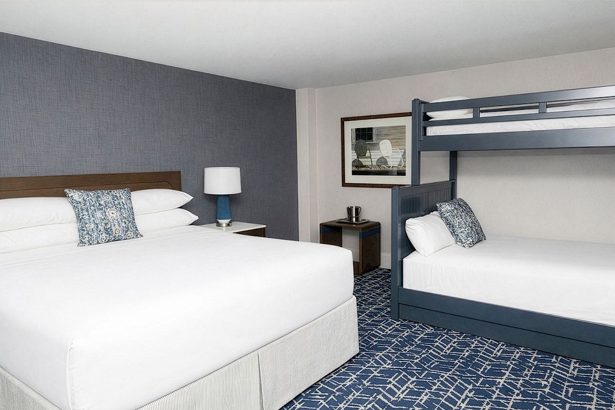 A hotel room with a king bed and a navy blue accent wall, plus a bunk bed setup on the right and nightstands with lamps.