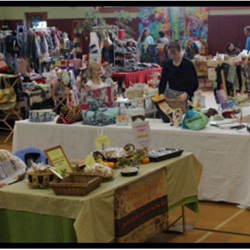 A community market with vendors selling various items at tables; people browsing and shopping.