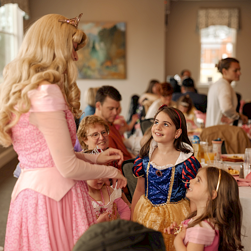 A princess party with kids in costumes, chatting and smiling around tables, festive snacks, and a warm, playful vibe.