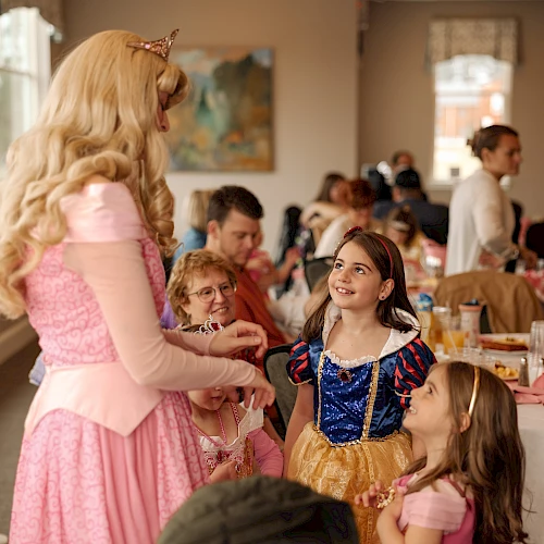 A princess party with kids in costumes, chatting and smiling around tables, festive snacks, and a warm, playful vibe.
