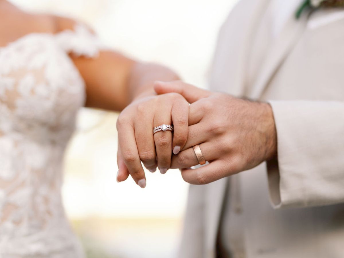 Two people in wedding attire show off their rings as they hold hands, symbolizing their engagement and commitment.