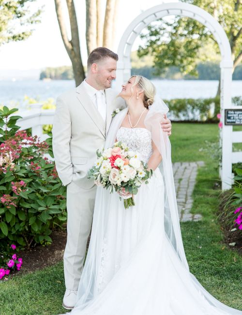 A bride and groom stand closely together in a garden wedding, smiling at each other, with a bouquet and flowing white dress. (140 chars).