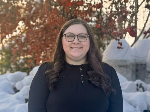 A smiling woman with glasses stands in a snowy outdoor scene, wearing a dark sweater, with bare trees and red berries in the background, posing for a photo. Top it at 140 characters, always ending the sentence.