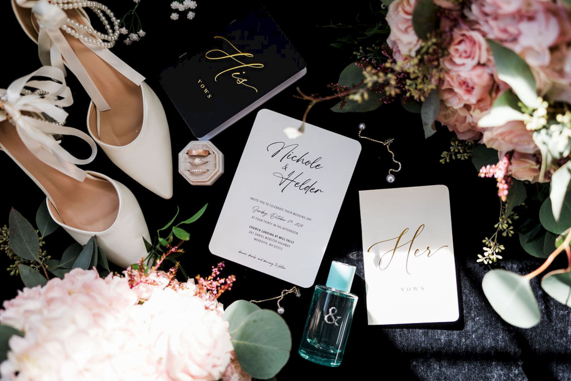 Wedding details laid out with heels, florals, and invitations; a chic, monochrome palette with gold accents, perfume bottle, and greenery.