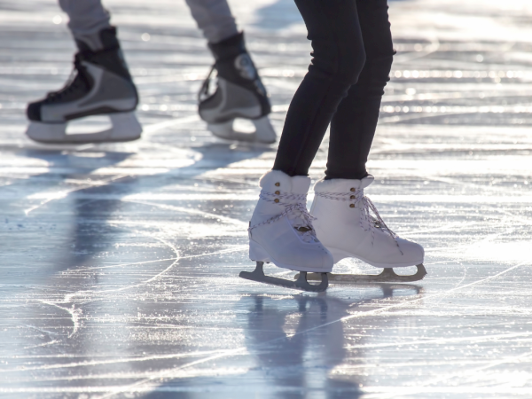Ice skaters gliding on a sunlit rink, close-up of white skates and reflective ice, motion and shadows creating a dynamic scene.