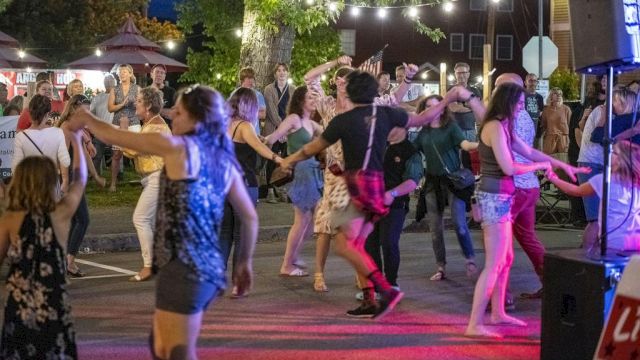 A lively outdoor dance party with people twirling, swapping partners, and enjoying string lights under a night market vibe.