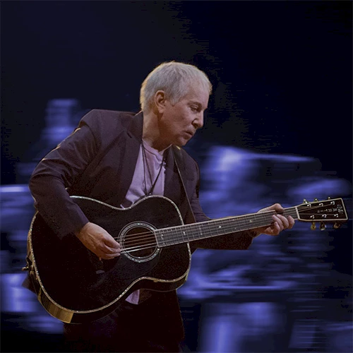 A man playing a black acoustic guitar on stage, blurred blue lights in the background.