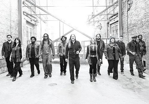 A group of people walking confidently down a snowy alley, leather jackets and casual wear, urban vibe, black‑and‑white photo.