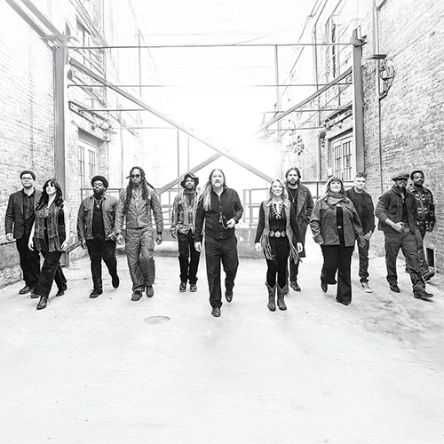 A group of people walking confidently down a snowy alley, leather jackets and casual wear, urban vibe, black‑and‑white photo.