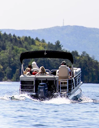 A boat with people cruising on a calm lake, mountains in the background under a clear sky, enjoying a sunny day.