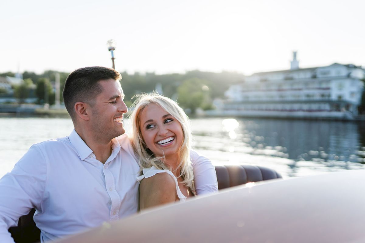 A happy couple sits on a boat by the water, smiling at each other as the sun glows on the harbor.