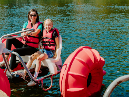 Two people wearing life jackets riding an aqua trike on a calm lake.