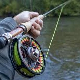 A person fishing, holding a rod and reel over a river, line cast, with a forested bank in the background.