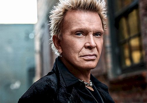 A stylish man with bleached blond spiky hair, leather jacket, standing in an alley with brick walls and a moody vibe.