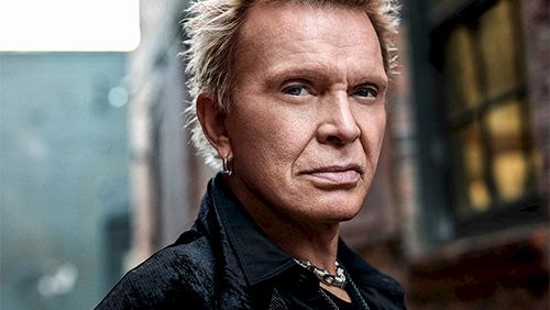 A stylish man with bleached blond spiky hair, leather jacket, standing in an alley with brick walls and a moody vibe.