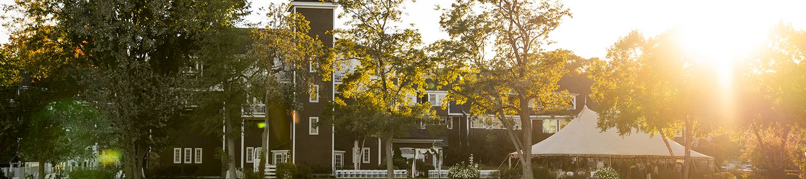 A lakeside town with trees, a brick building and clock tower along the shore, bathed in warm sunset light on calm water.
