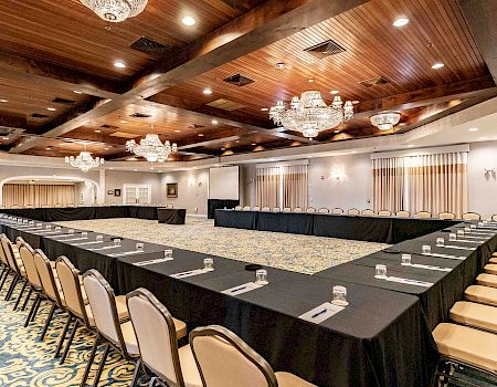 A large conference room with U-shaped black-table setup, beige chairs, chandeliers, carpeted floor, and nameplates/water glasses at each seat.