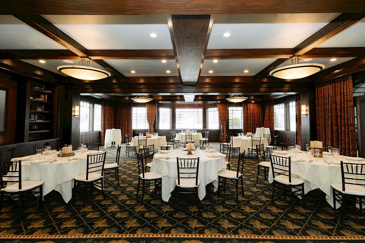 A formal dining room with round tables, white tablecloths, elegant chairs, warm lighting, and dark wood paneling, ready for a banquet.